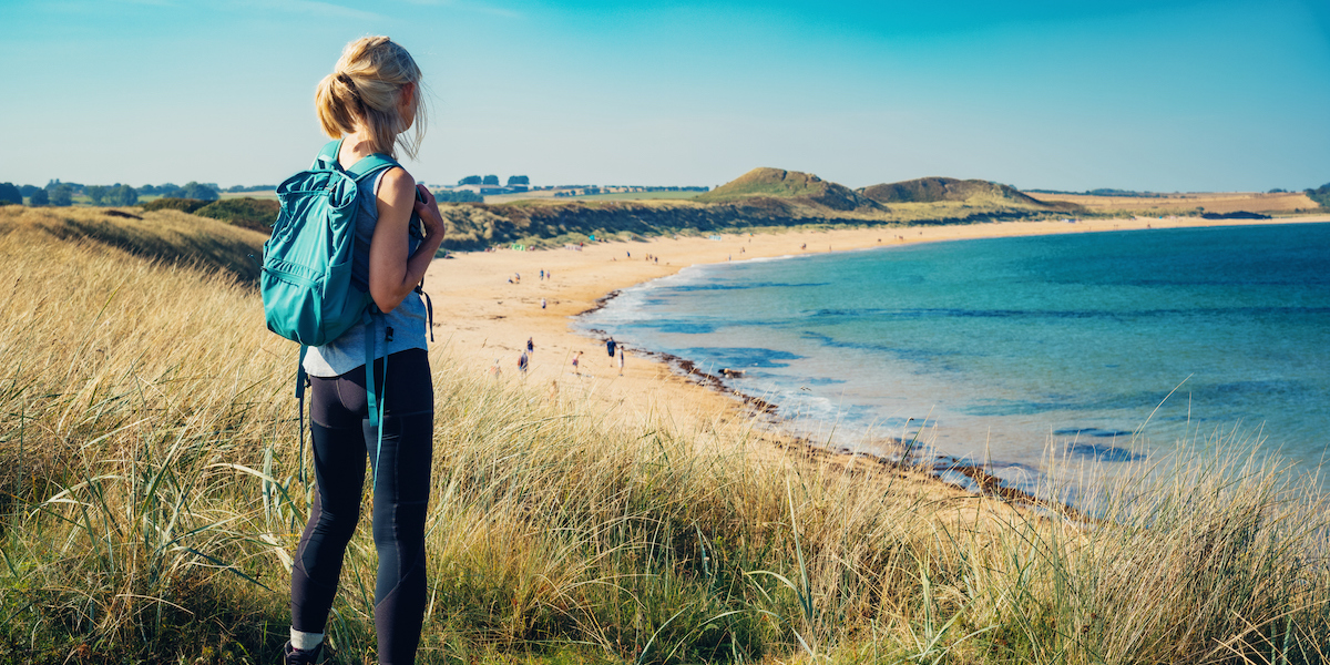 Femail hiker looking towards a sandy beach.